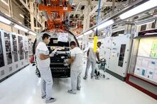 Foto: Drei Personen arbeiten an einem Fahrzeug in einer Fabrikhalle. Im Hintergrund Maschinen und technische Geräte.